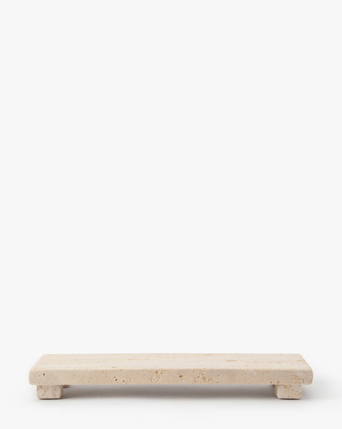 The Beige Travertine Footed Serving Board, with small legs and a minimalist design, is shown slightly elevated on a plain white background, highlighting its elegant travertine stone surface, by McGee & Co.