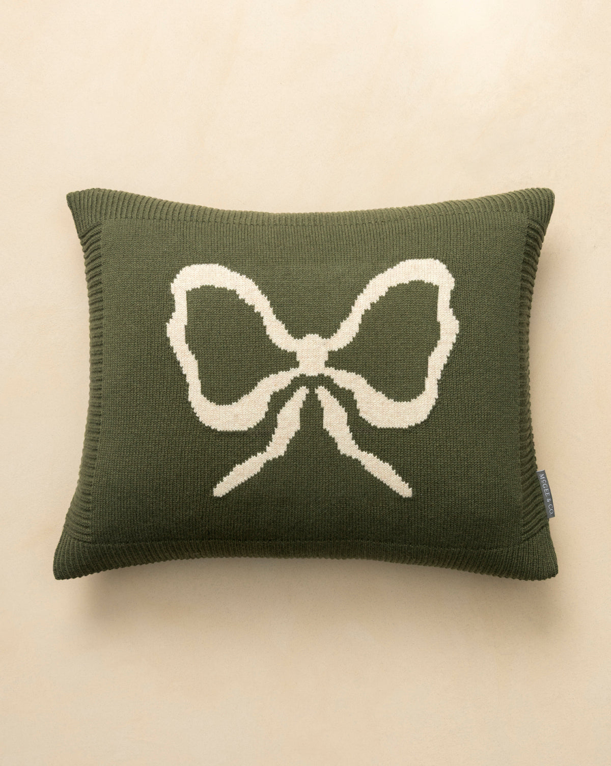 The Bella Pillow Cover is rectangular, dark green, and features a large cream bow in the center. Its cozy knit texture makes it perfect for holiday layering, by McGee & Co.