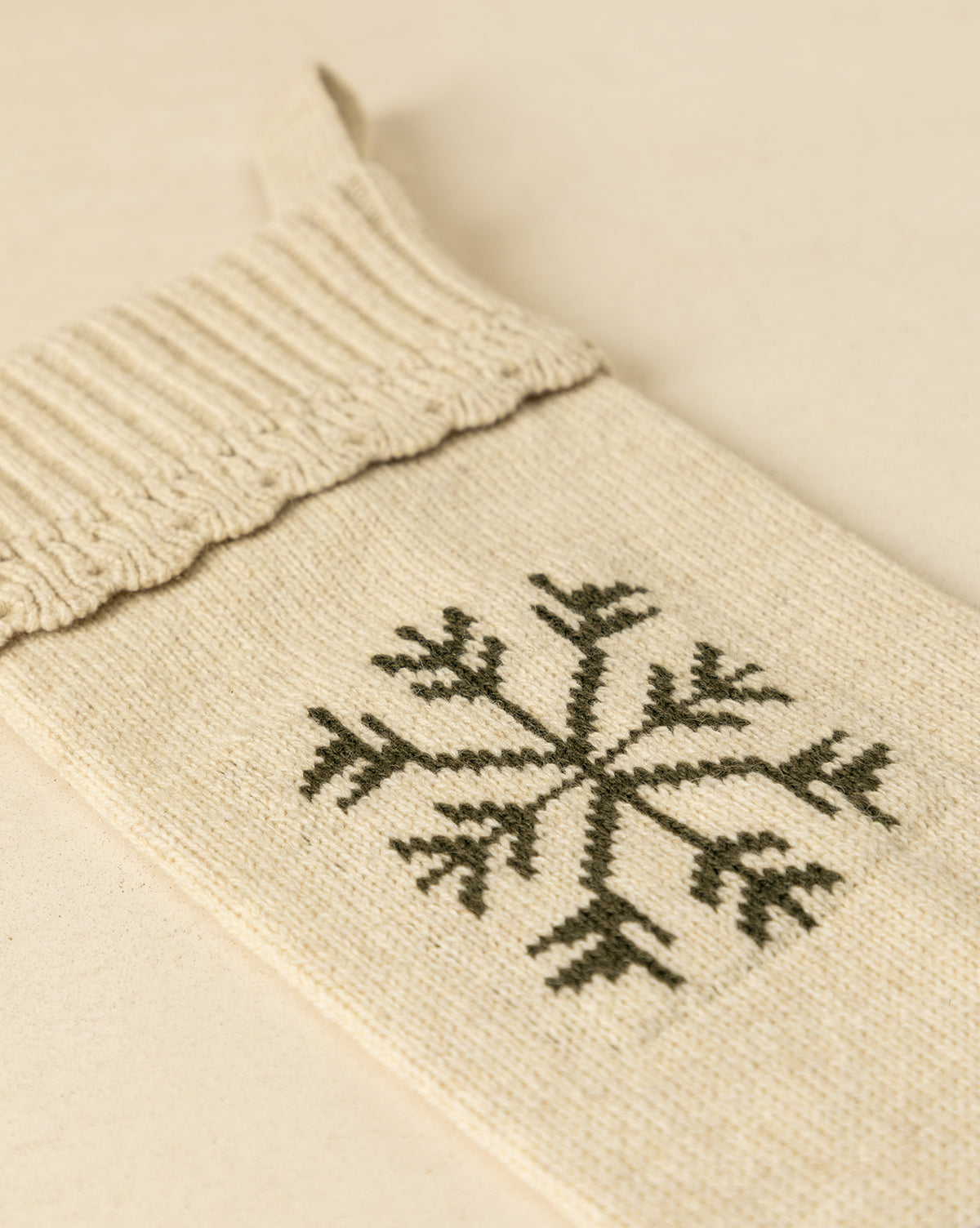 The Bella Scalloped Stocking with Snowflake, in cream knit with a dark green snowflake design, is displayed on a beige surface—an ideal festive addition to your holiday mantel decor, by McGee & Co.
