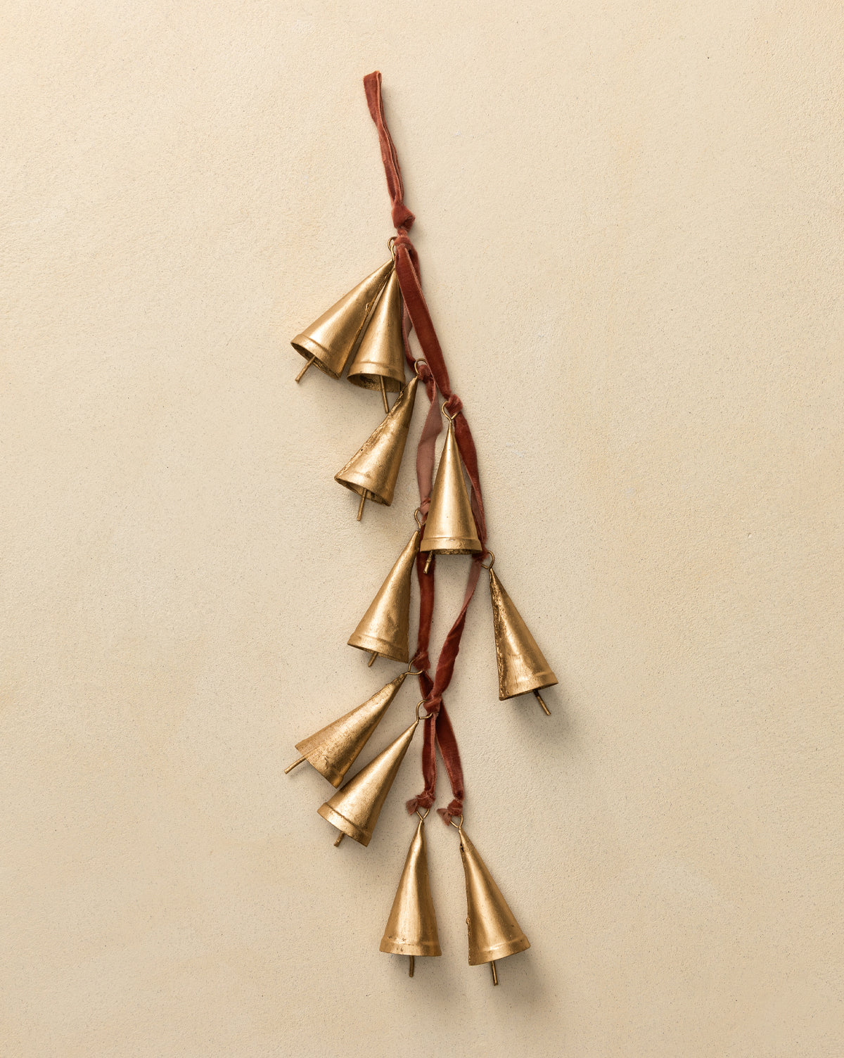 The Bells on Velvet Ribbon Door Hanger features nine small gold cone-shaped metal bells suspended from rich velvet, creating a festive accent against any beige wall, by McGee & Co.