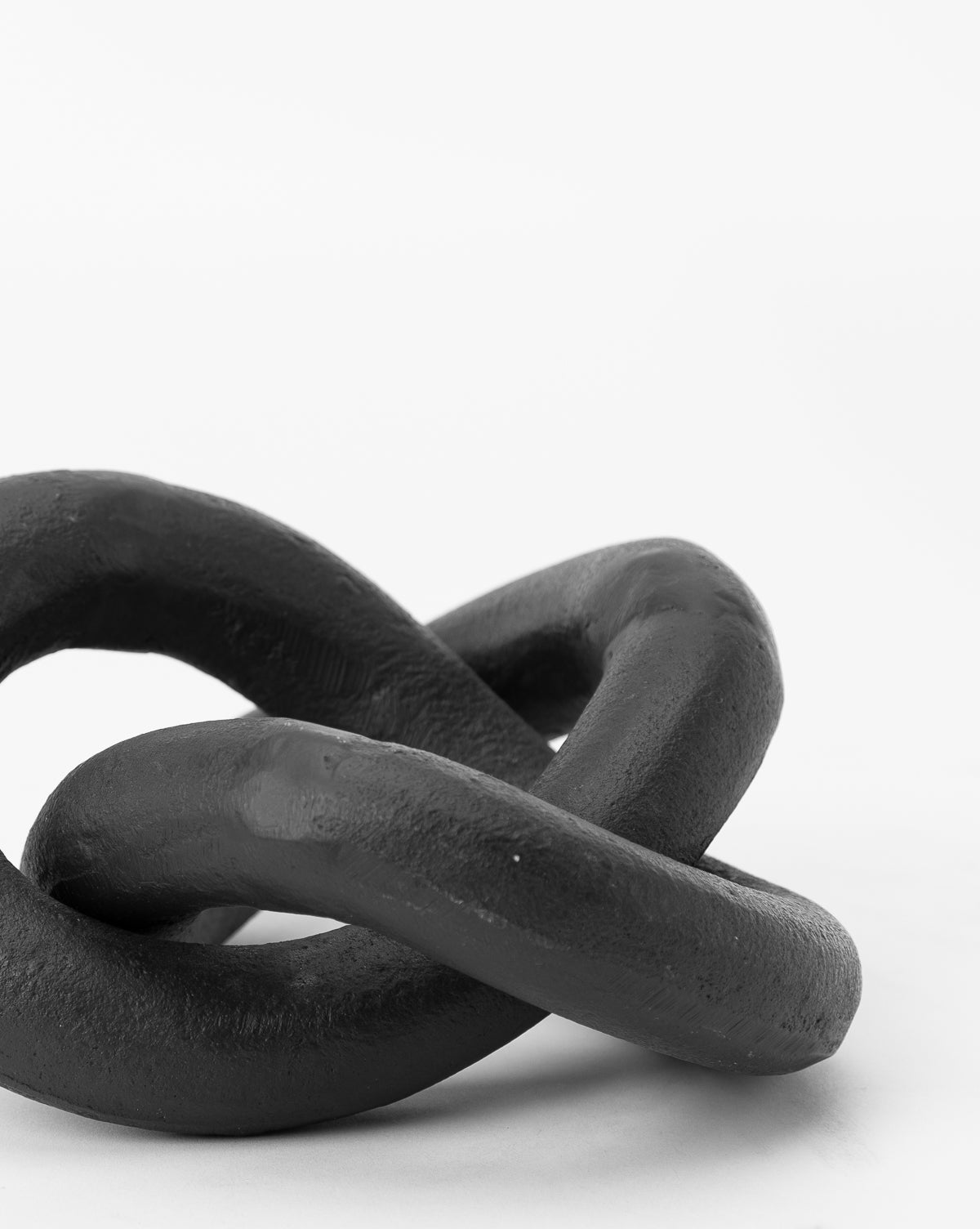 A close-up of the Black Infinity Loop shows two thick, black metal links interlocked against a plain white background—a bold, modern home accessory and striking piece of metal decor.