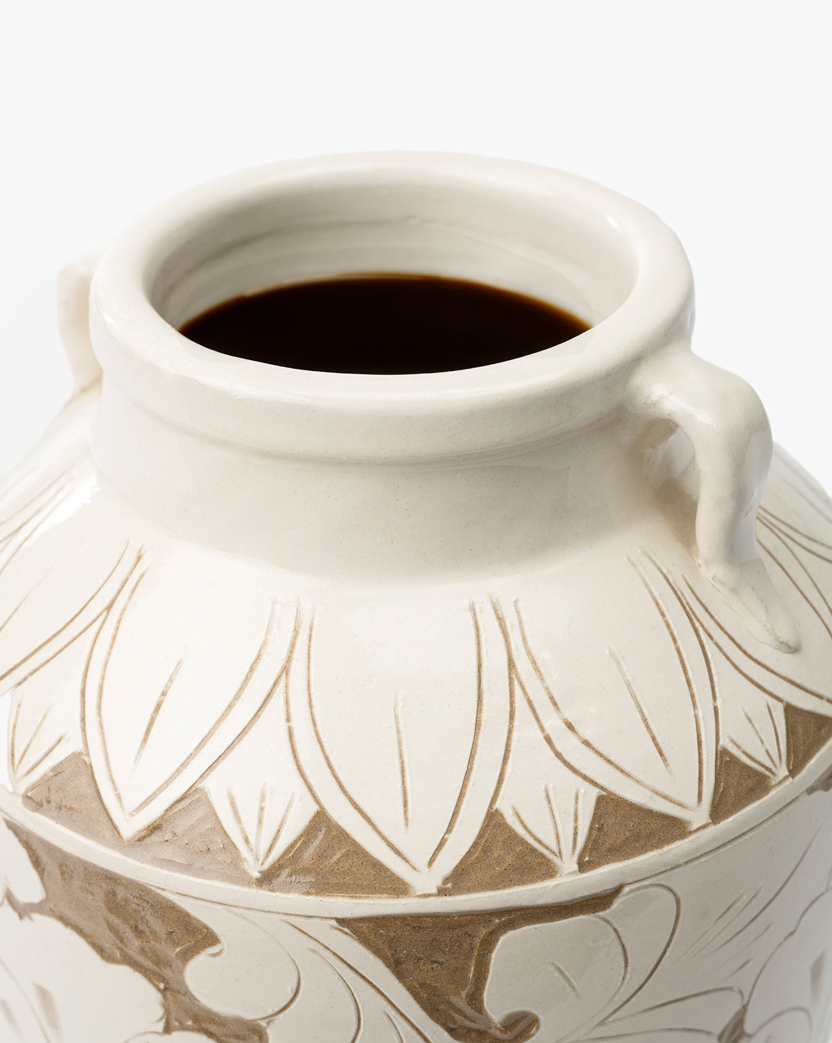 A close-up of the cream-colored Blaise Vase, handmade with an open mouth, two small side handles, and an etched leaf pattern—partially filled with a dark liquid for an elegant touch to your home decor, by McGee & Co.