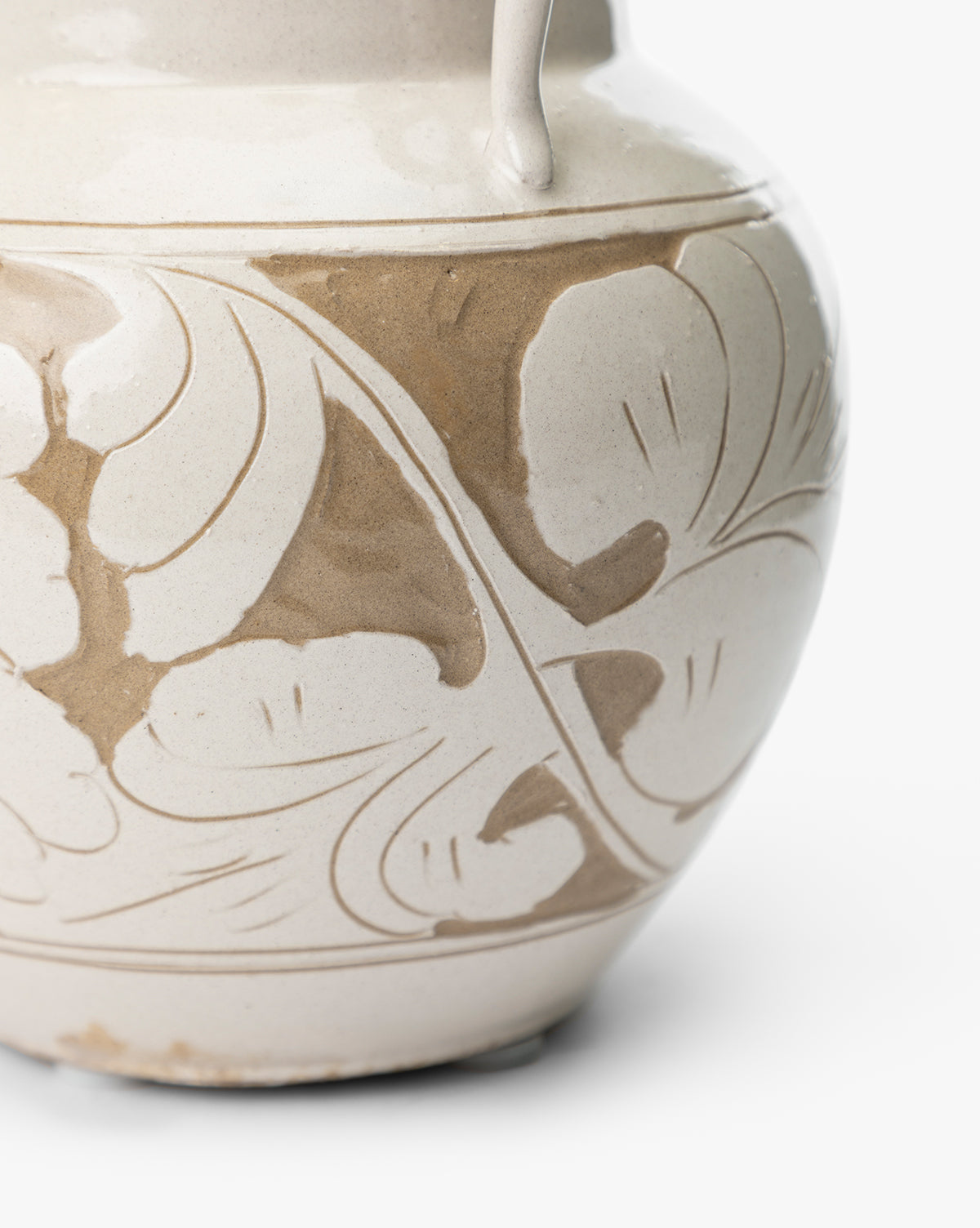A close-up of the Blaise Vase, handmade with a light beige glaze and an abstract floral pattern in darker tan curving around its rounded surface, making it a unique home decor piece, by McGee & Co.