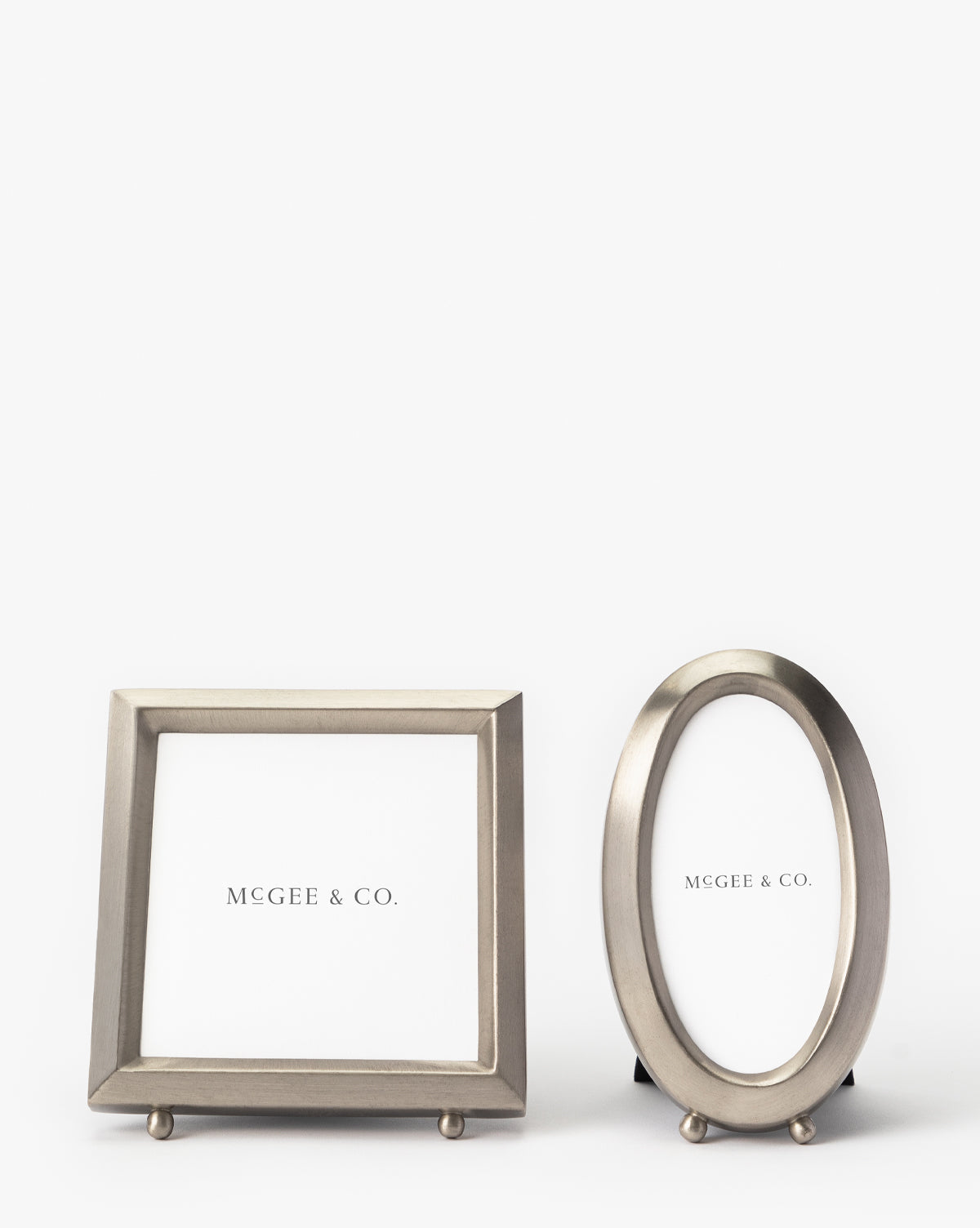 The Blanche Pewter Picture Frame, shown in both oval and rectangular shapes with small round feet, features a sophisticated design and MGEE & CO. placeholder text against a white background.