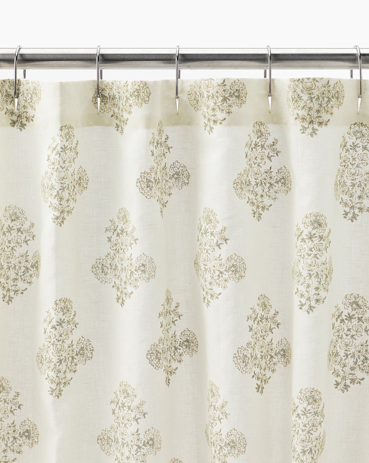 The Block Print Shower Curtain features a cream color with a subtle gold floral pattern, hanging from silver hooks on a metal rod. Lightweight and slightly sheer, it adds charming vintage decor to any bathroom.