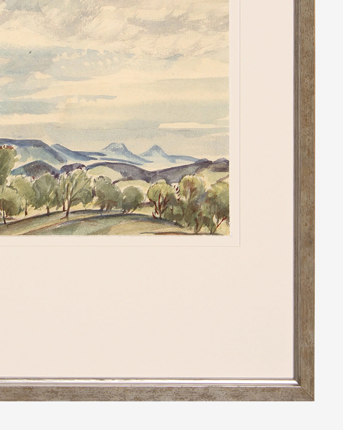 Blue Sky & Trees is a watercolor giclee print featuring a whimsical landscape of hills, scattered trees, and a cloudy sky, partially displayed in a silver-finished wood frame with a white mat.