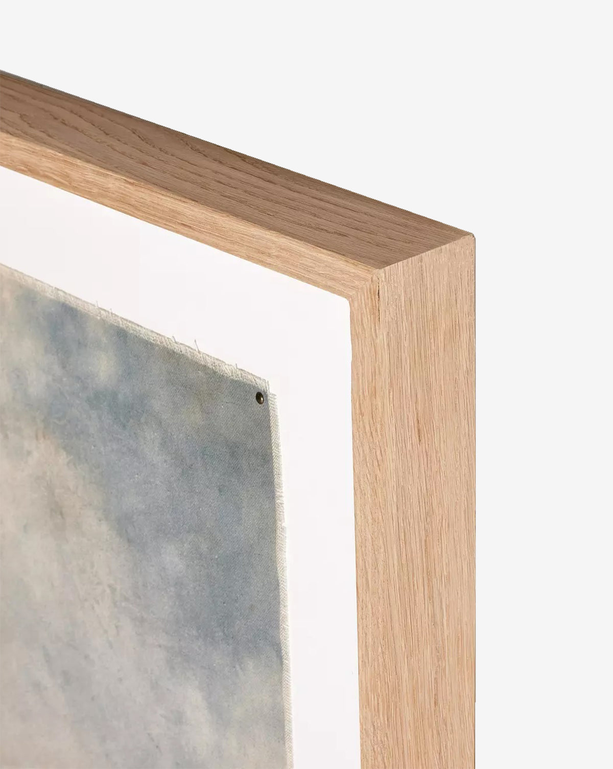 Close-up of a white oak frame with a white mat, showing the corner of Blue Spendor by Aileen Fitzgerald, a textured gray-blue giclee print secured with a tack against a plain, light background.