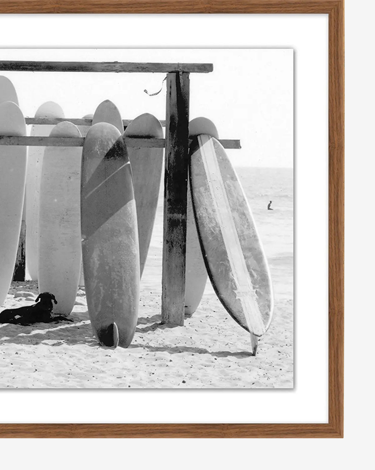 Boards at the Ready—a black and white photo of surfboards upright in sand beneath a rack, with a dog resting in the shade and ocean view—captures classic surf culture. Makes an ideal giclée print for any beach lover, by McGee & Co.