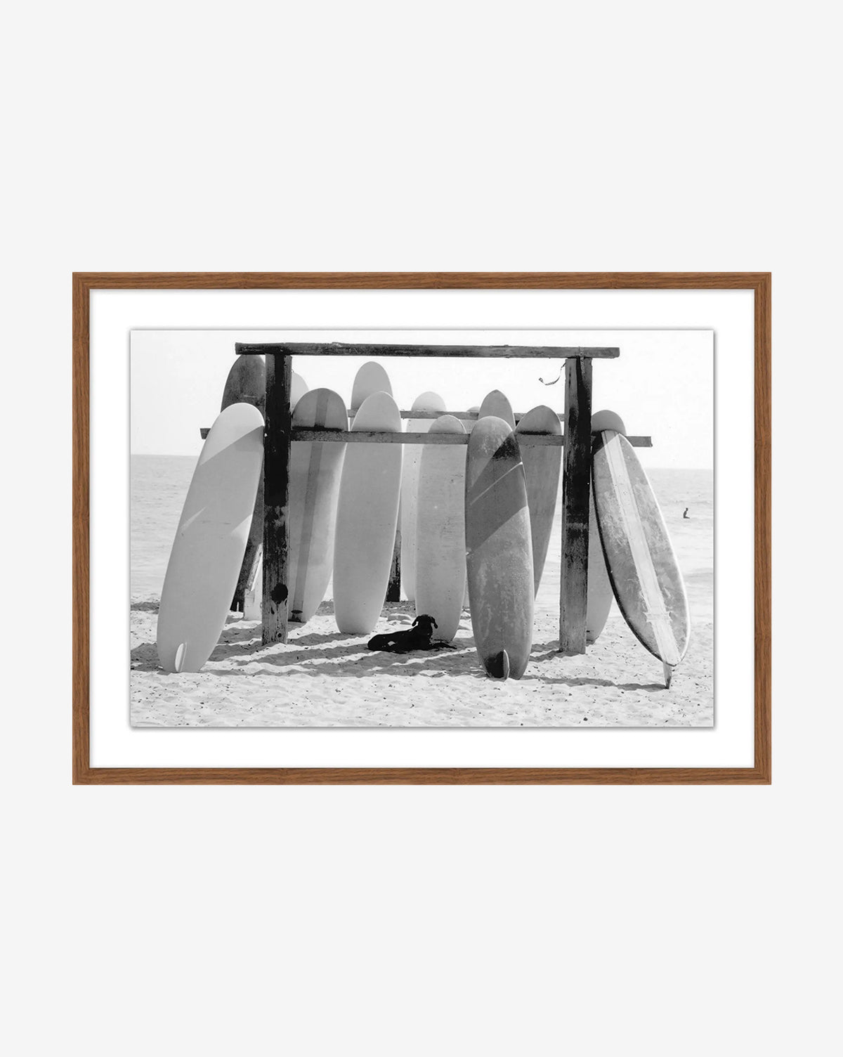 Boards at the Ready—a black and white photo of surfboards upright in a beachside wooden rack, the ocean in view, framed in a brown wooden frame—captures iconic surf culture, by McGee & Co.