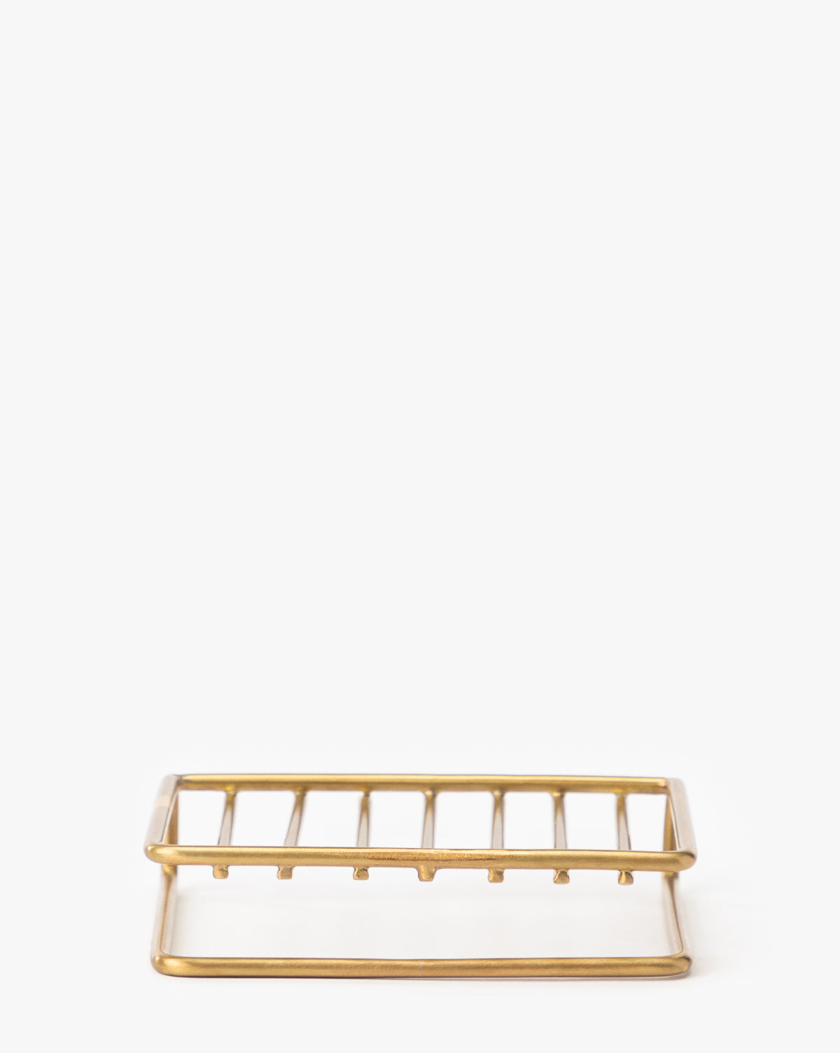 The Brass Soap Dish features a simple rectangular design with parallel bars and open sides, crafted from brass-finished metal—an elegant addition to any bathroom countertop.