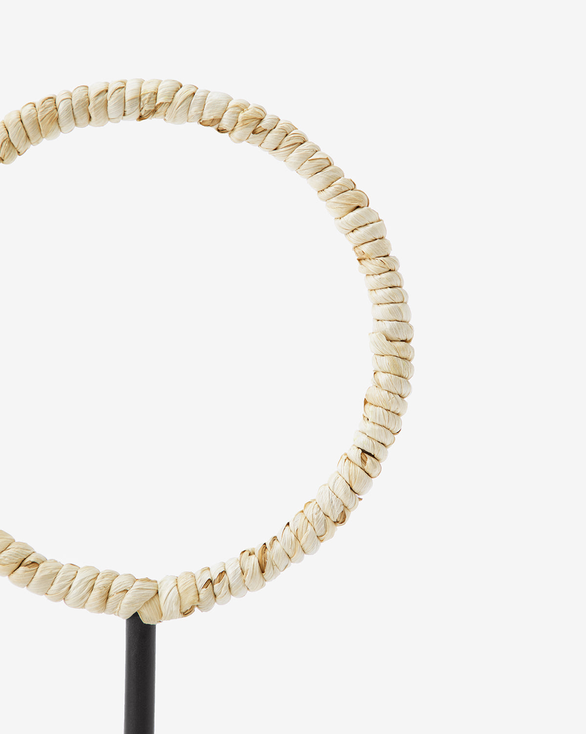 A close-up of the Brayden Woven Object shows its circular form made from twisted natural fibers with a corn husk texture, displayed on a black stand against a white background.