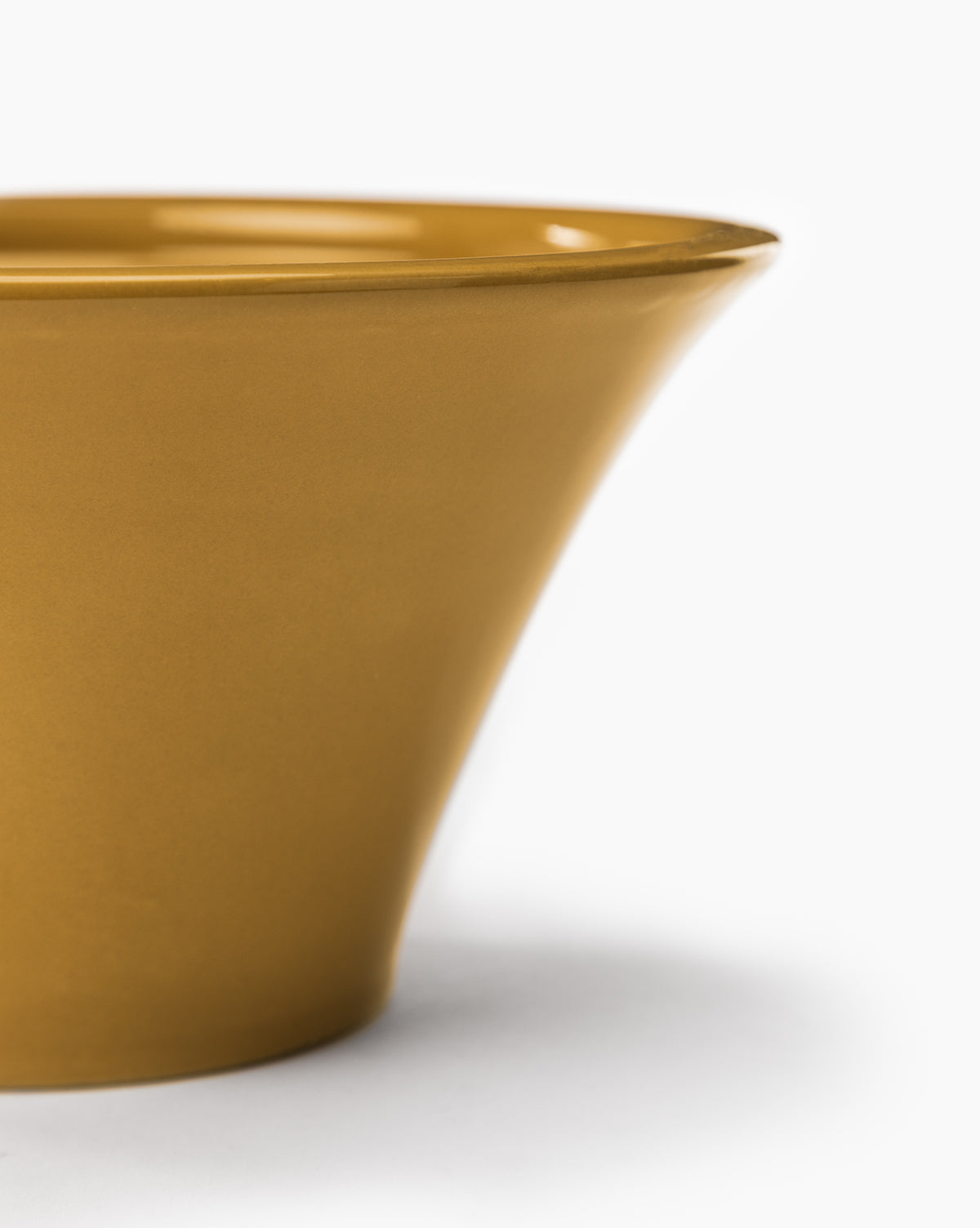 Close-up of the rim and side of the glossy Brennan Serving Bowl in marigold, set against a white background. Only part of this ceramic bowl is visible, adding a vibrant touch to your kitchen decor, by McGee & Co.