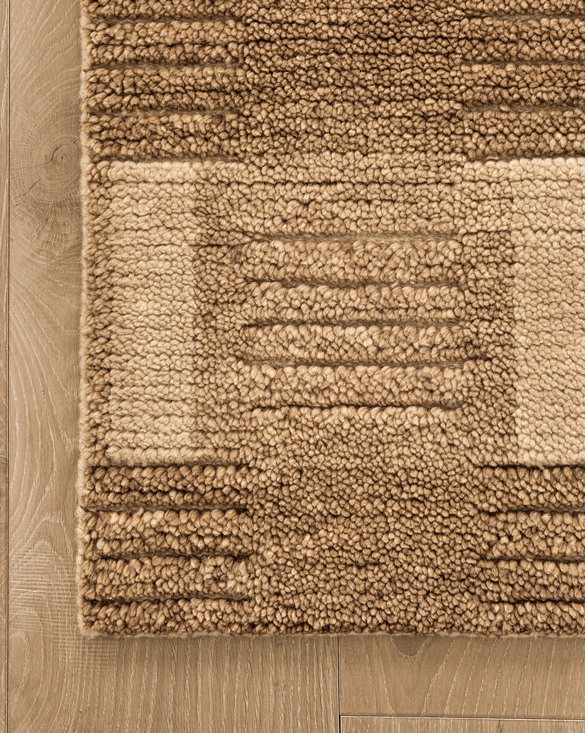 A close-up of the Brenner Hand-Knotted Wool Rug, showcasing its textured beige and brown geometric pattern with raised rectangular and linear designs, placed on a light wood floor for added depth, by McGee & Co.