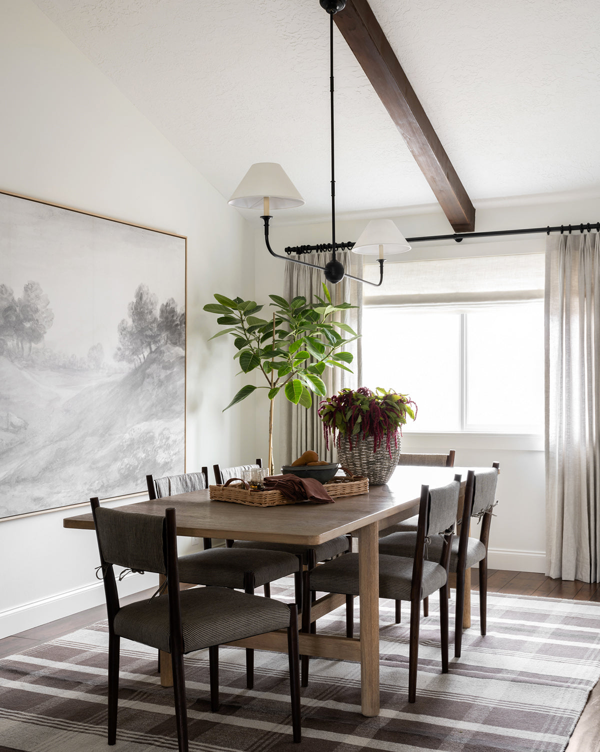 A modern dining room with a wooden table, six gray chairs, large wall art, a potted plant, the Orton Handwoven Wool Rug, and a window with beige curtains that let in natural light, by McGee & Co.