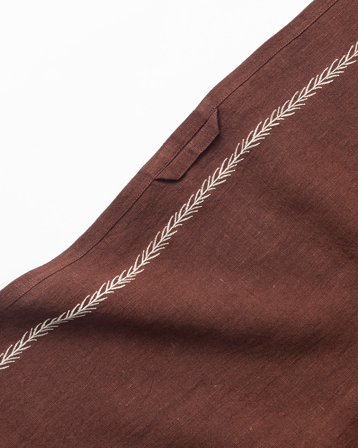 A close-up of the Broadleaf Tea Towel, featuring a brown fabric with an embroidered leaf border and a small rectangular loop—an elegant kitchen accessory set against a white background, by McGee & Co.