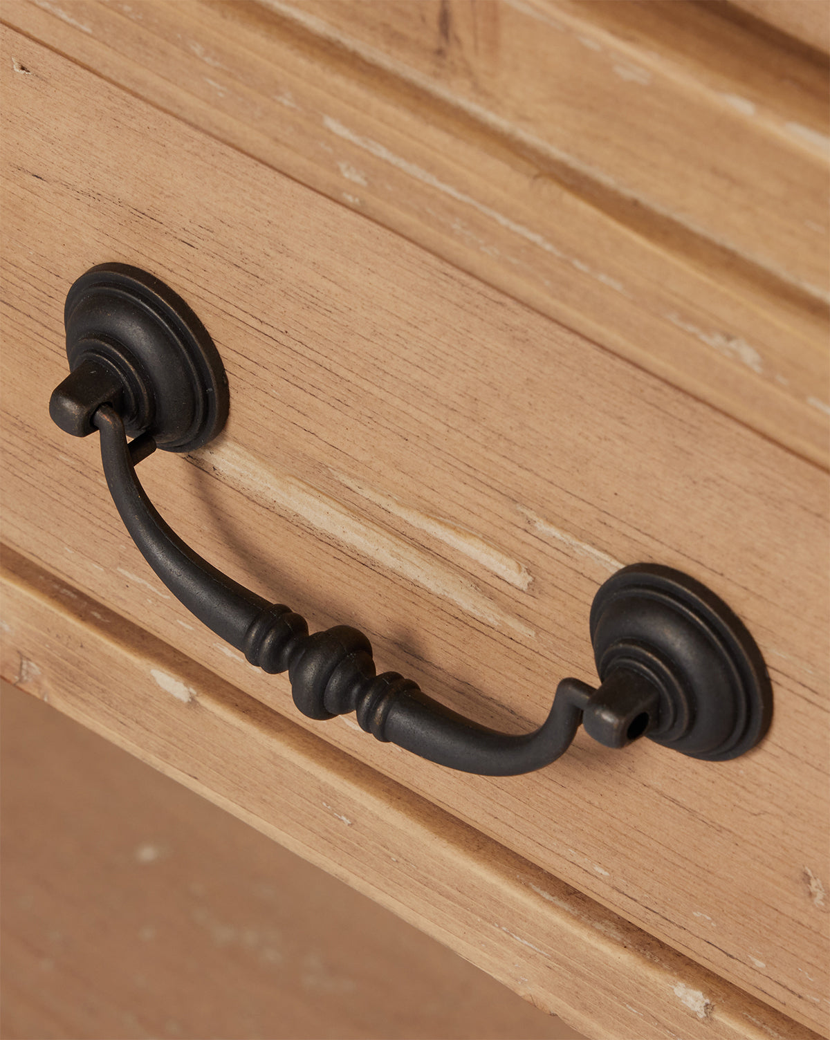 A close-up of a dark distressed copper handle fixed to the Bryn Cabinet’s light, natural-finish solid pine drawer by McGee & Co.