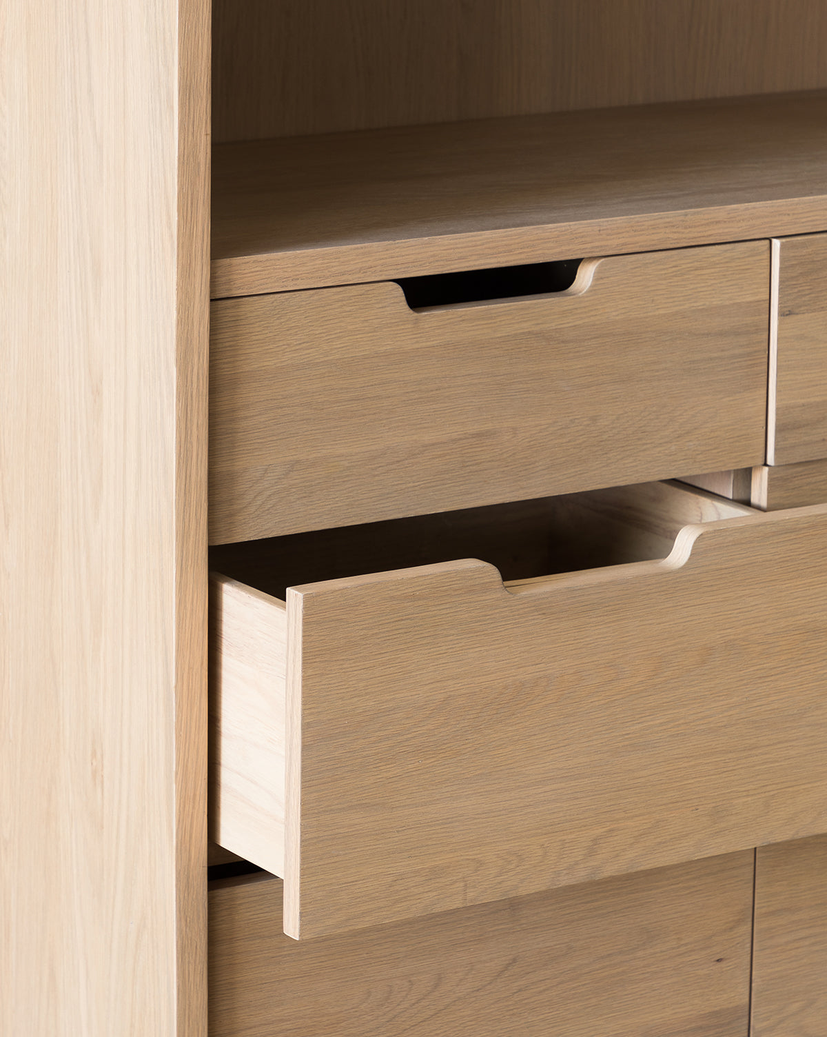 A close-up of the Burnham Cabinet shows a partially open drawer with minimalist, handleless cutouts, light wood finish, and clean modern lines—ideal for dining room storage by McGee & Co.