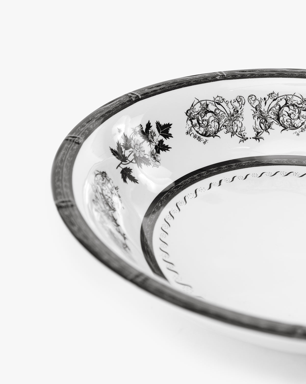 A close-up of the Calanthe Melamine Serving Bowl, featuring intricate black floral and scroll patterns on a decorative white rim, is photographed against a plain white background, by McGee & Co.
