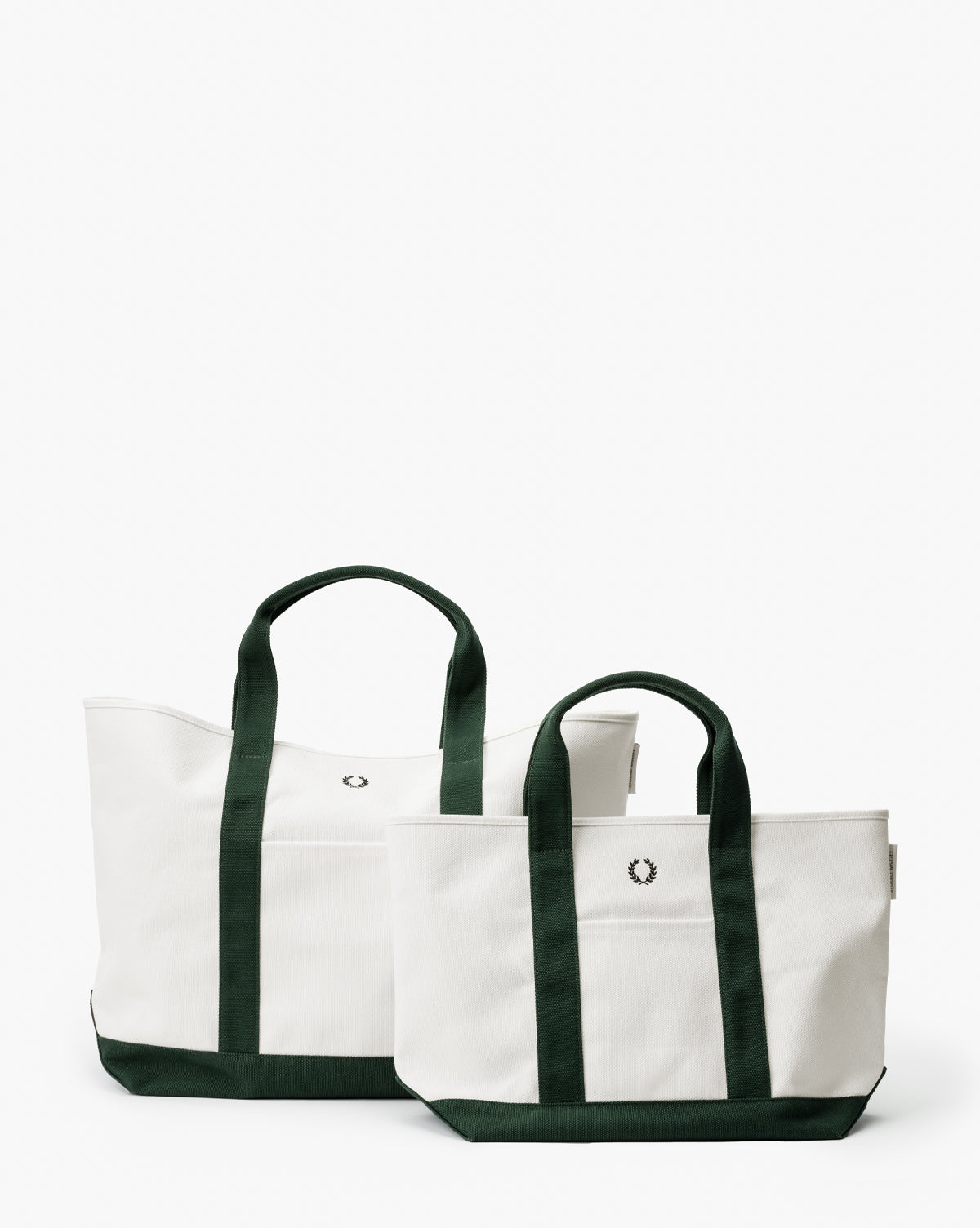 Two white Canvas Laurel Totes with dark green handles and bottoms, each featuring a small embroidered laurel wreath. The larger tote is placed behind the smaller one, creating a stylish, layered look, by McGee & Co.