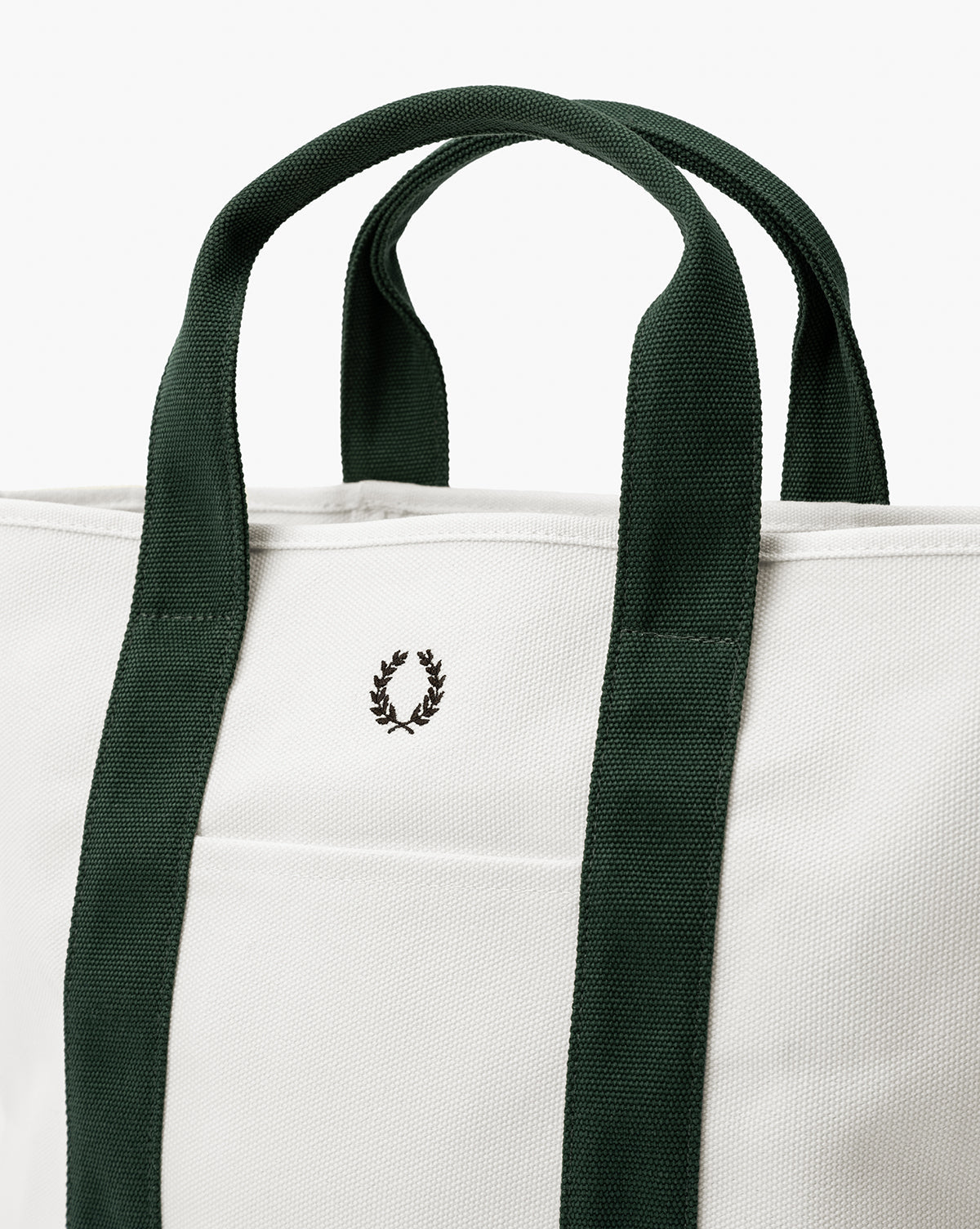 A close-up of the Canvas Laurel Tote highlights its white canvas, dark green handles, and a small black laurel wreath logo embroidered on the front pocket—making it perfect for everyday use, by McGee & Co.