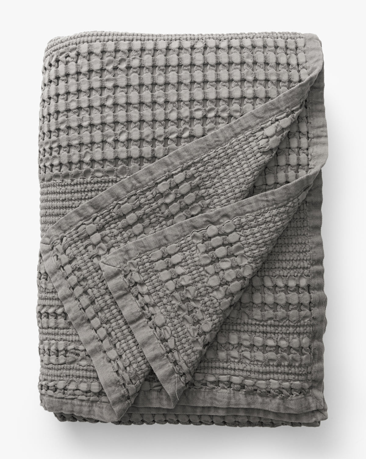 The Penedo Carnel Gray Waffle Blanket features a textured, grid-like woven pattern with raised details and is shown on a white background. A flipped corner reveals the matching inner texture. McGee & Co.