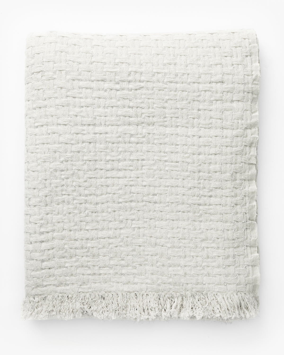 The Caroline Kids Blanket by Indigo Craft is an off-white, textured woven blanket with fringe at the bottom edge, shown folded on a white background by McGee & Co.