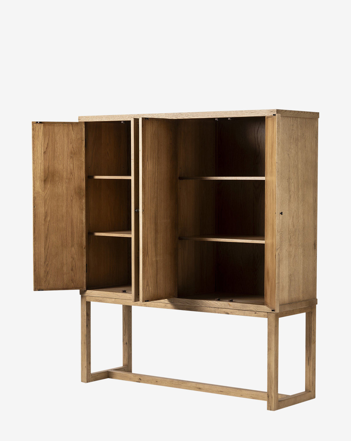 The Carrington Cabinet, made from worn oak with bronze-finished hardware, stands on a simple rectangular frame. One of its two doors is open, showing three interior shelves, all set against a plain white background by McGee & Co.