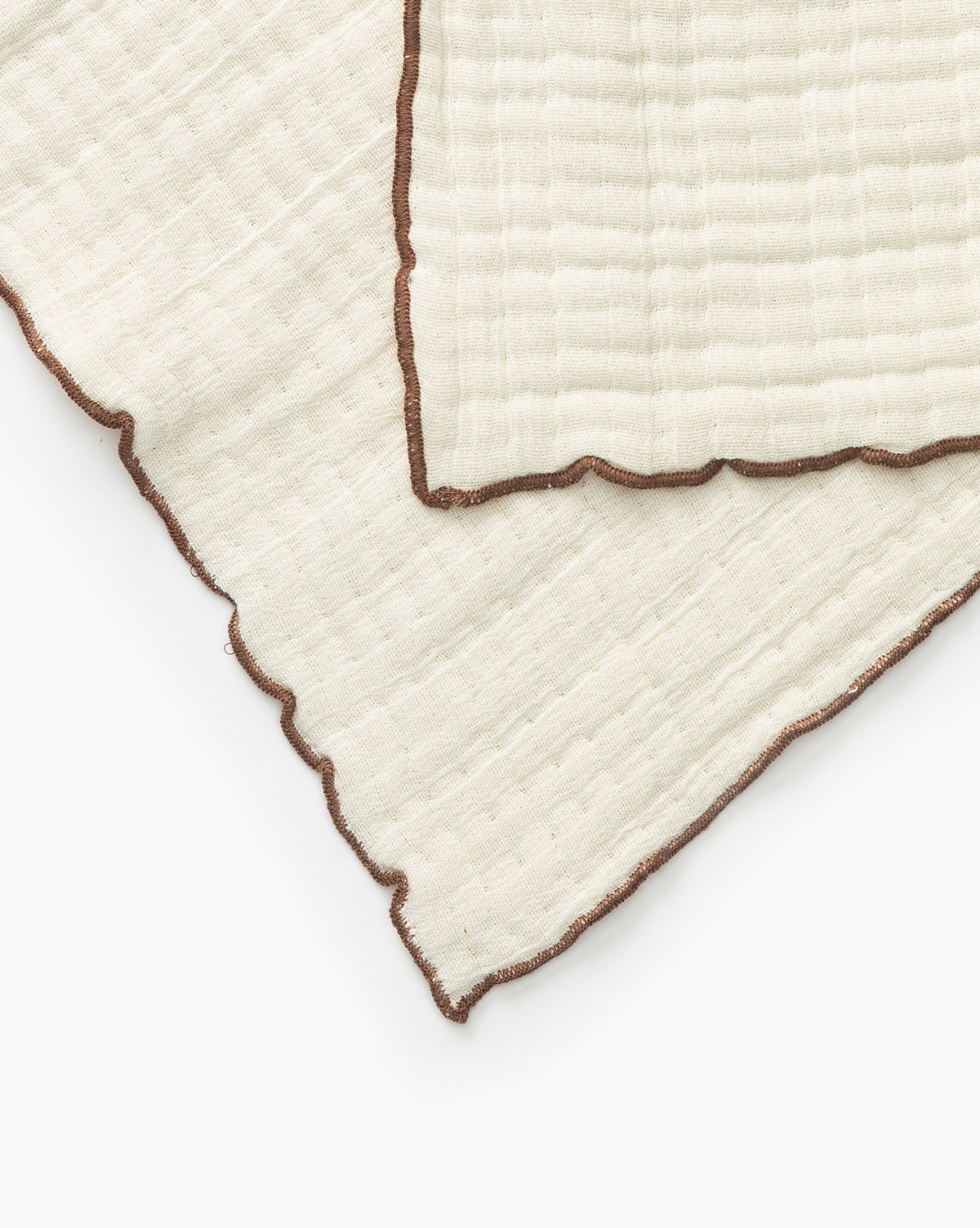 Close-up of two overlapping Cassidy Waffle Hand Towels in cream cotton with wavy brown stitched edges, shown on a white background.