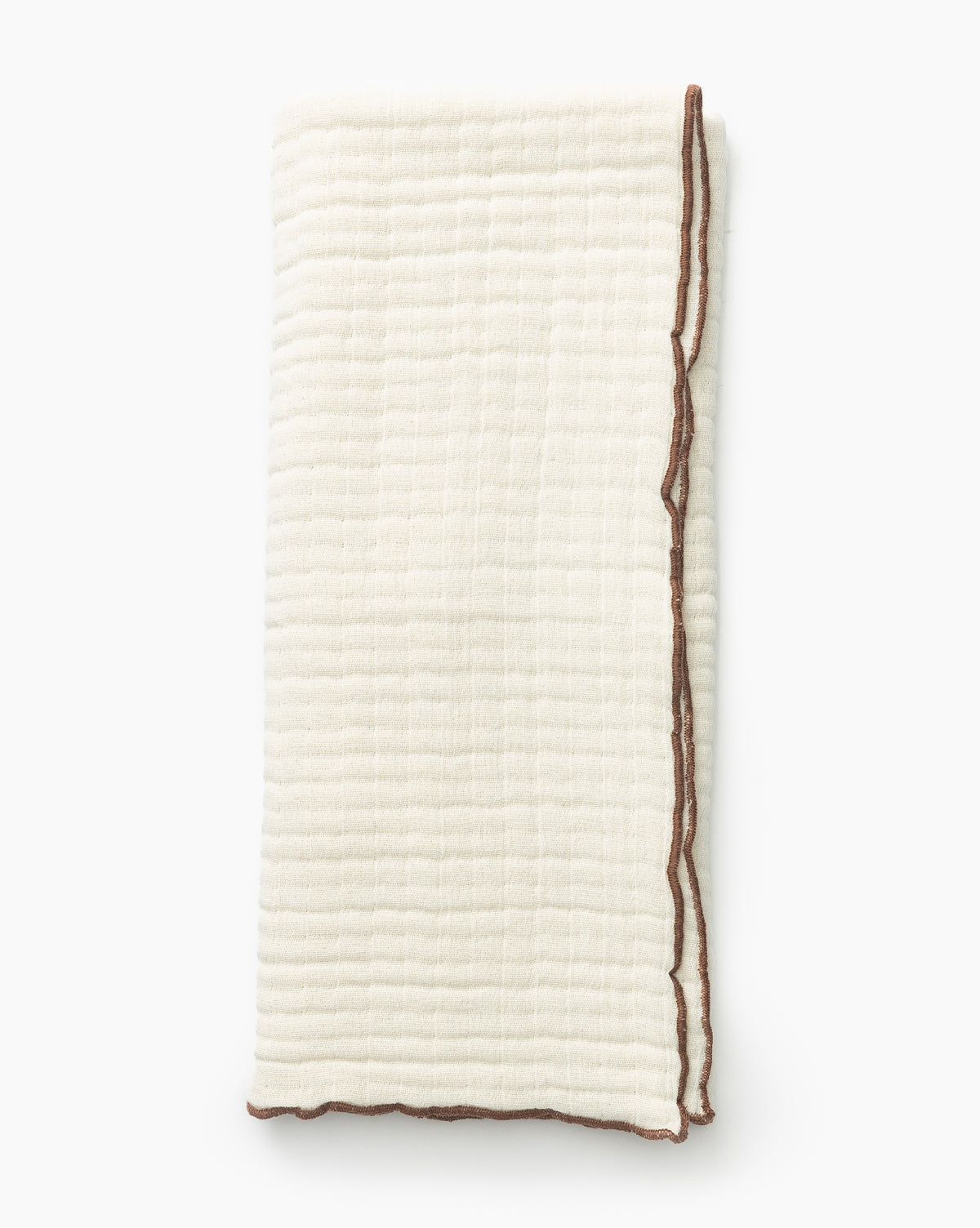 The Cassidy Waffle Hand Towel is a folded, off-white cotton towel featuring a textured grid-like waffle weave and brown stitched edging, shown against a plain white background.