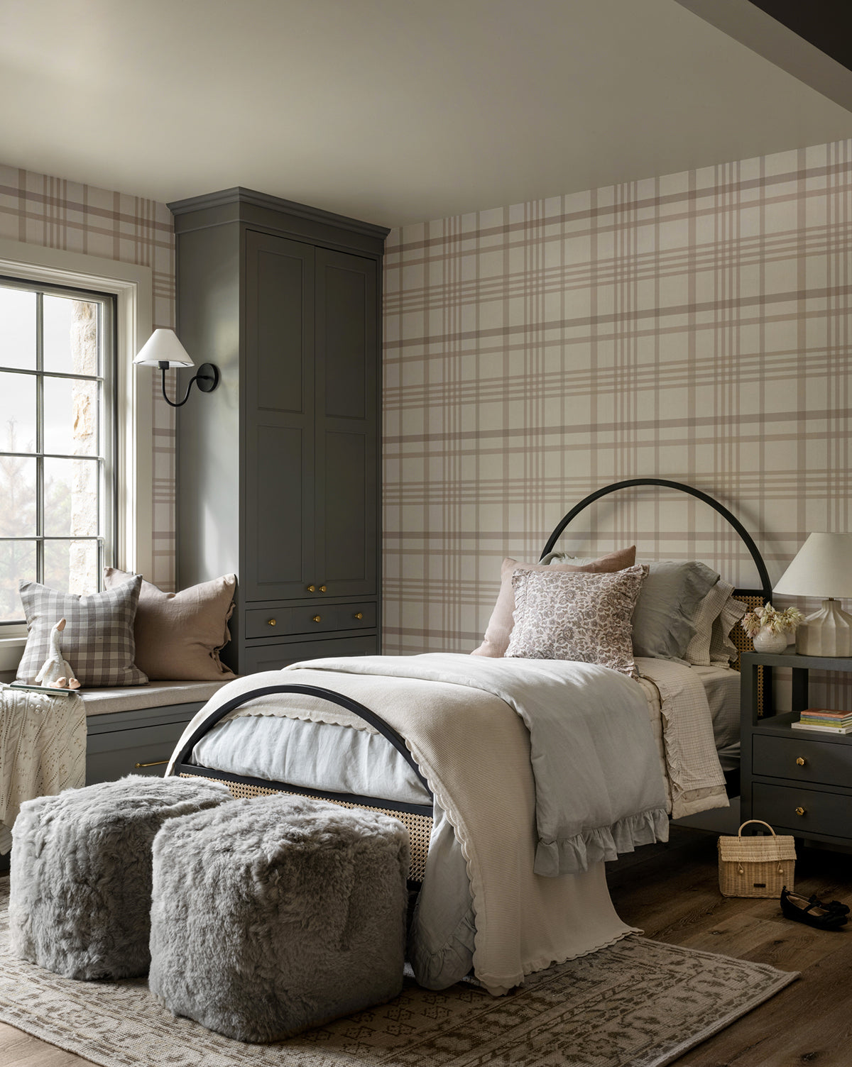 A cozy bedroom features a single bed with the Ruffle Linen Duvet Cover in gray and beige, plaid wallpaper, gray cabinets, a window seat with pillows, two furry gray ottomans, a nightstand with lamp, and neutral decor.