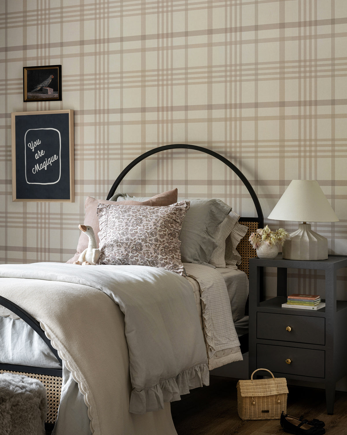 A cozy bedroom with plaid wallpaper, a neatly made bed with gray and beige bedding, pillows, and a stuffed bunny. On the gray nightstand sits the Veneto Table Lamp with its fluted base, along with flowers and books; wall art and a chalkboard hang above by McGee & Co.