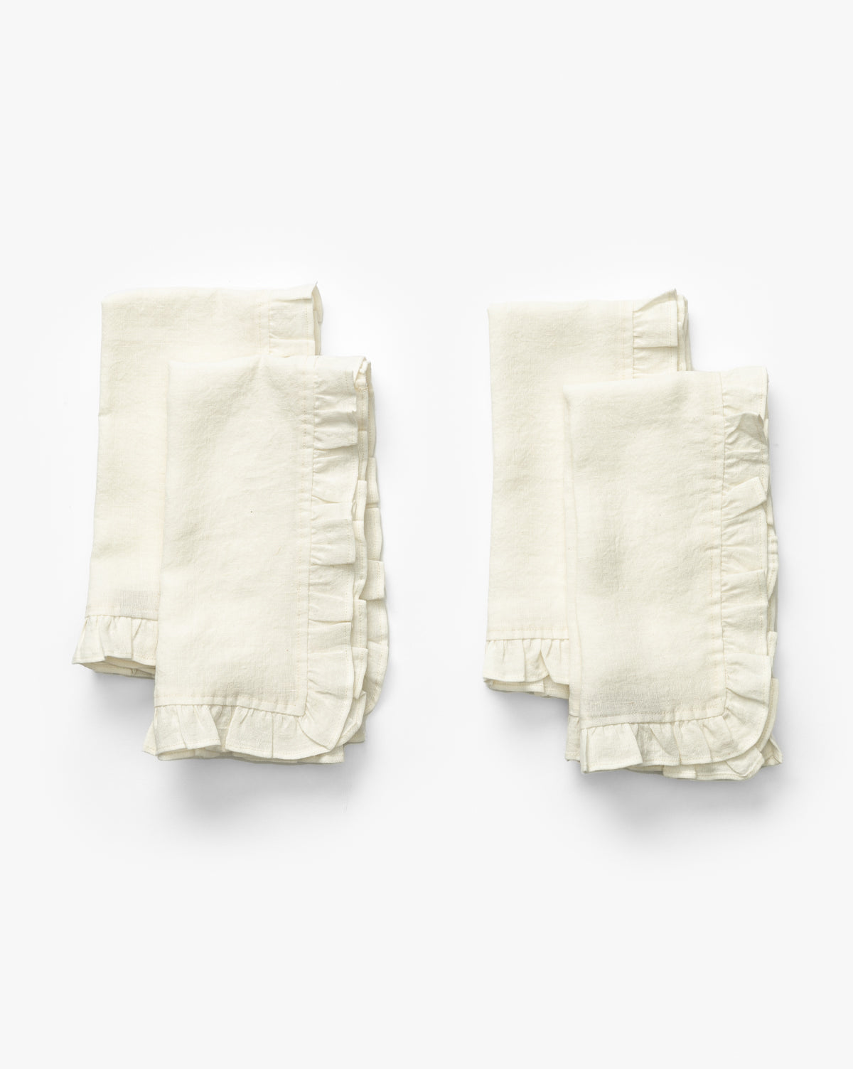 A set of four Catania Linen Napkins, off-white with delicate ruffled edges, is folded and arranged in two pairs on a plain white background by McGee & Co.