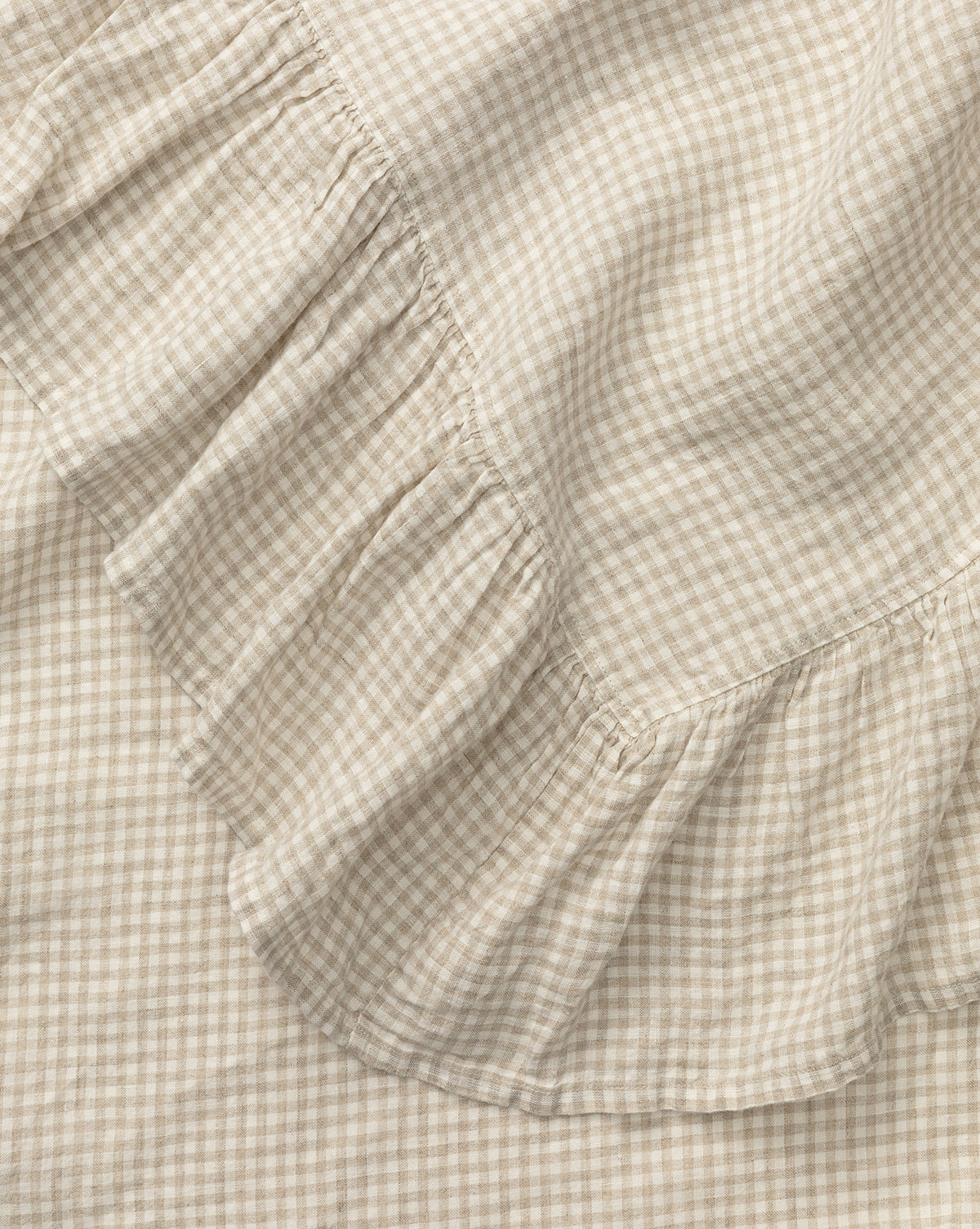 A close-up of the Catania Linen Ruffle Tablecloth in beige and white gingham, showcasing its soft, textured small checks and ruffled edge, by McGee & Co.