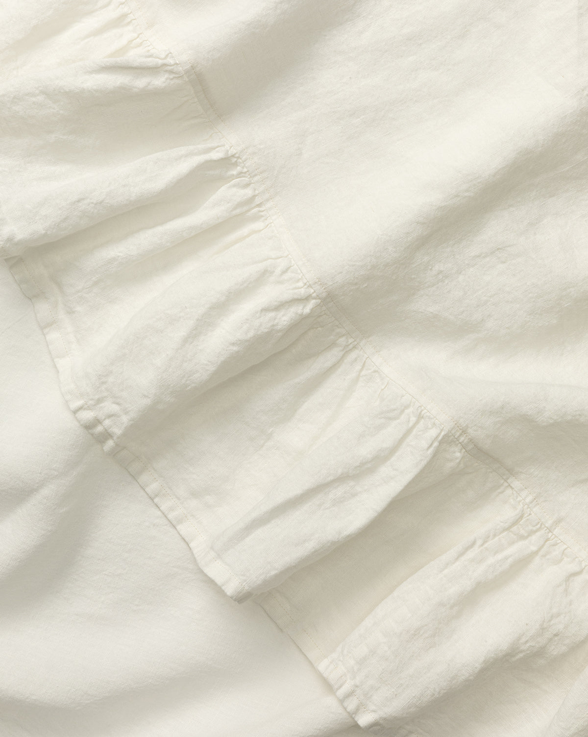 Close-up of the Catania Linen Ruffle Tablecloth in white, featuring a diagonal ruffled seam that highlights its soft texture and gentle folds, by McGee & Co.