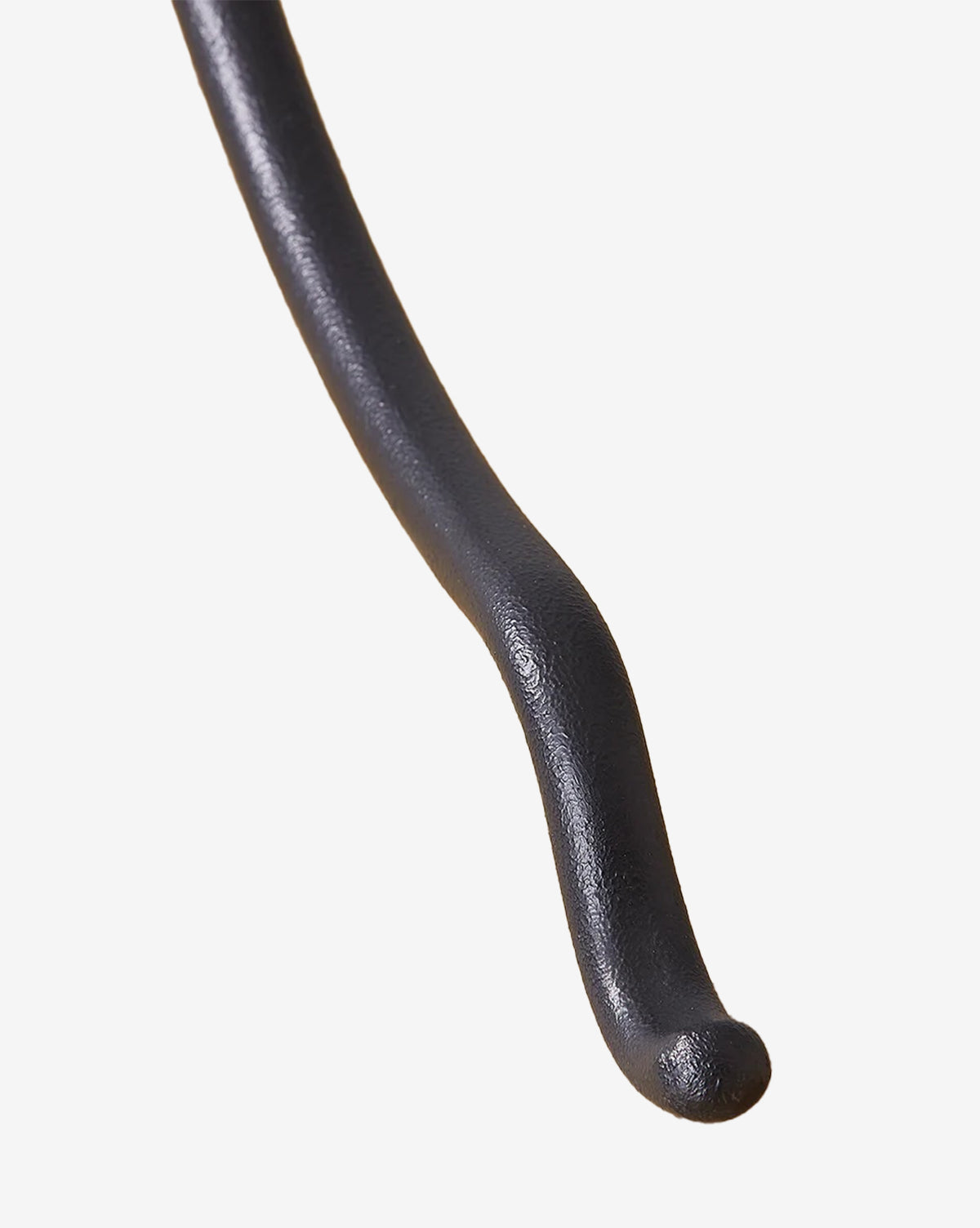 A close-up of a curved, black, textured object against a white background, reminiscent of the forged iron arm featured on the Cedar Floor Lamp by McGee & Co.