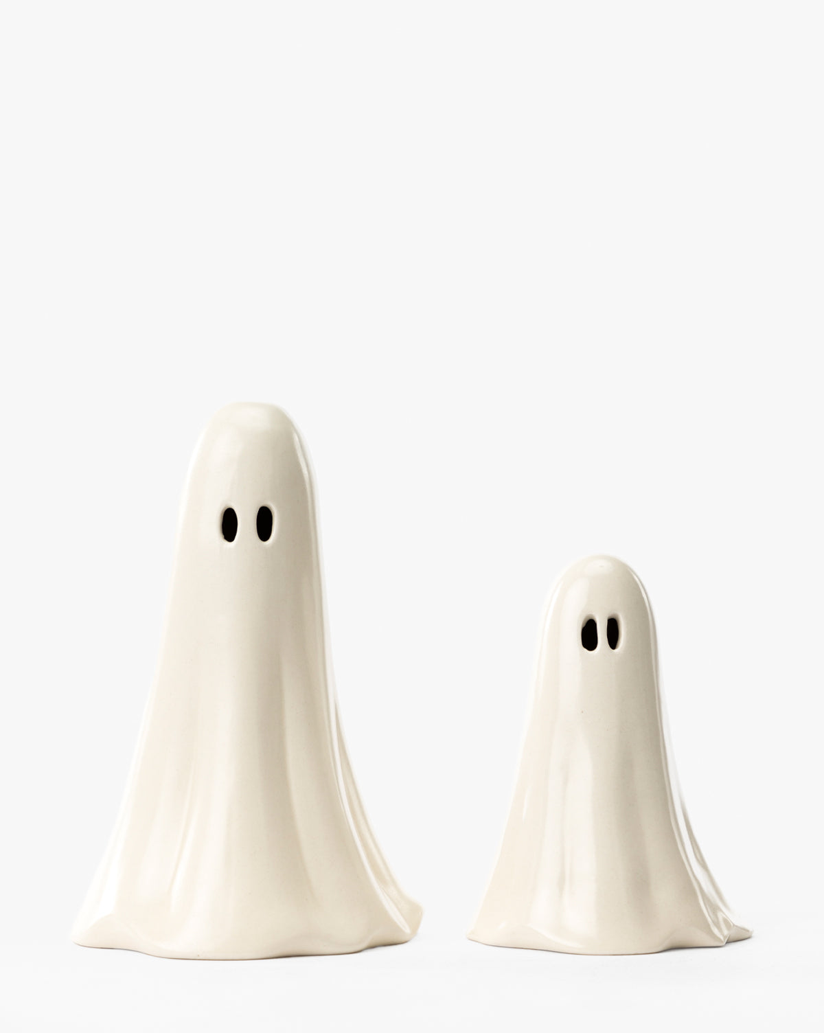Two Ceramic Ghost Figures—one tall, one short—with smooth white surfaces and black oval eyes stand together, perfect as charming Halloween decor or spooky home accents, by McGee & Co.