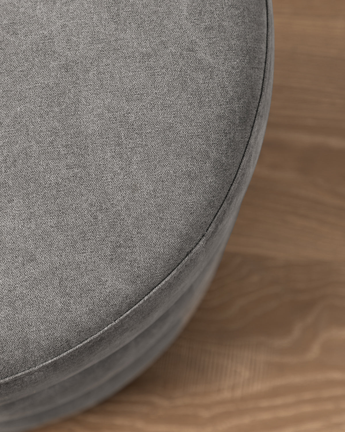 A close-up of the Channel Ottoman features its round, quilted gray design on a light brown wooden floor, adding a touch of midcentury style, by McGee & Co.