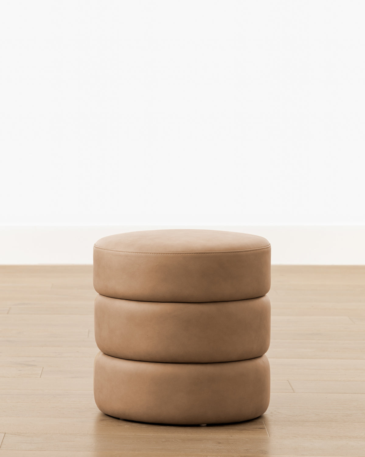 The Channel Ottoman is a round, tan ottoman featuring three stacked cushiony layers and subtle quilted details, adding midcentury charm to any space, by McGee & Co.