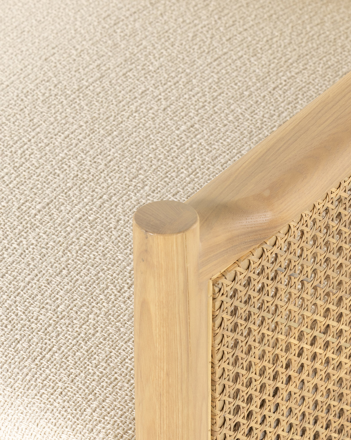 Close-up of the Channing Lounge Chair, featuring a light wood frame and woven rattan panel inspired by Parisian design. The corner post and woven detail stand out, with the chair set on a textured beige fabric surface, by McGee & Co.