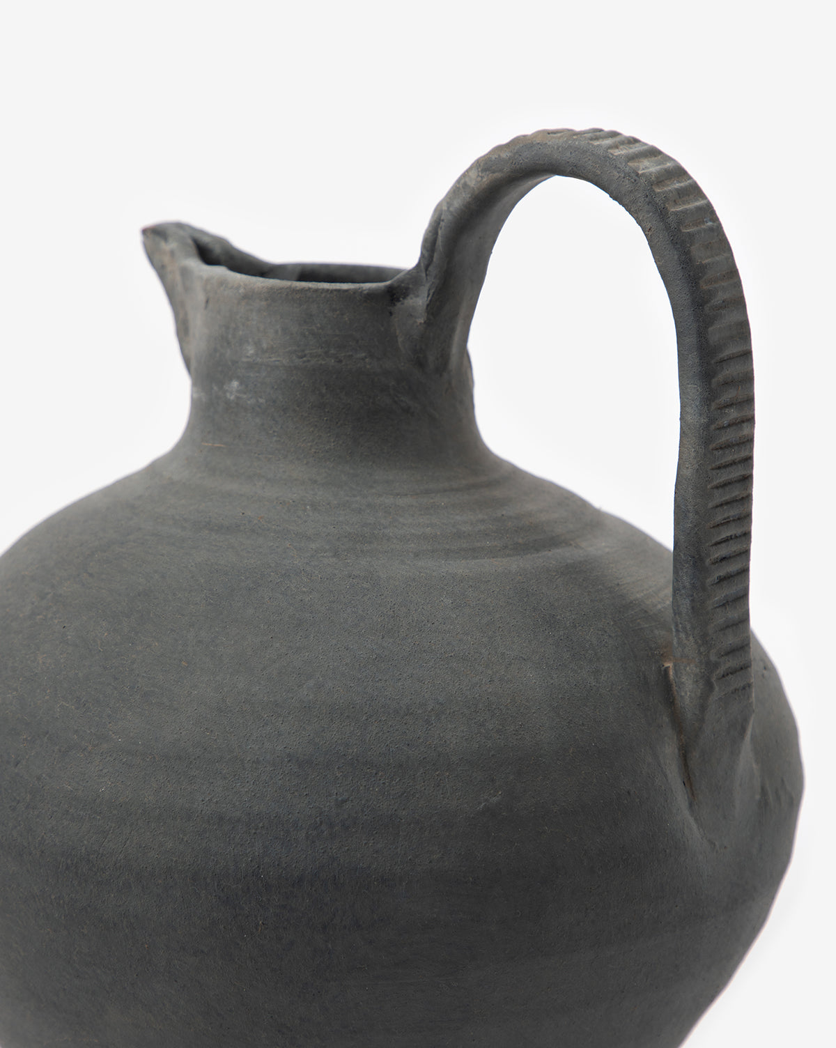 A handmade Charcoal Terracotta Jug with a textured handle and narrow spout is shown in close-up, elegantly set against a plain white background.