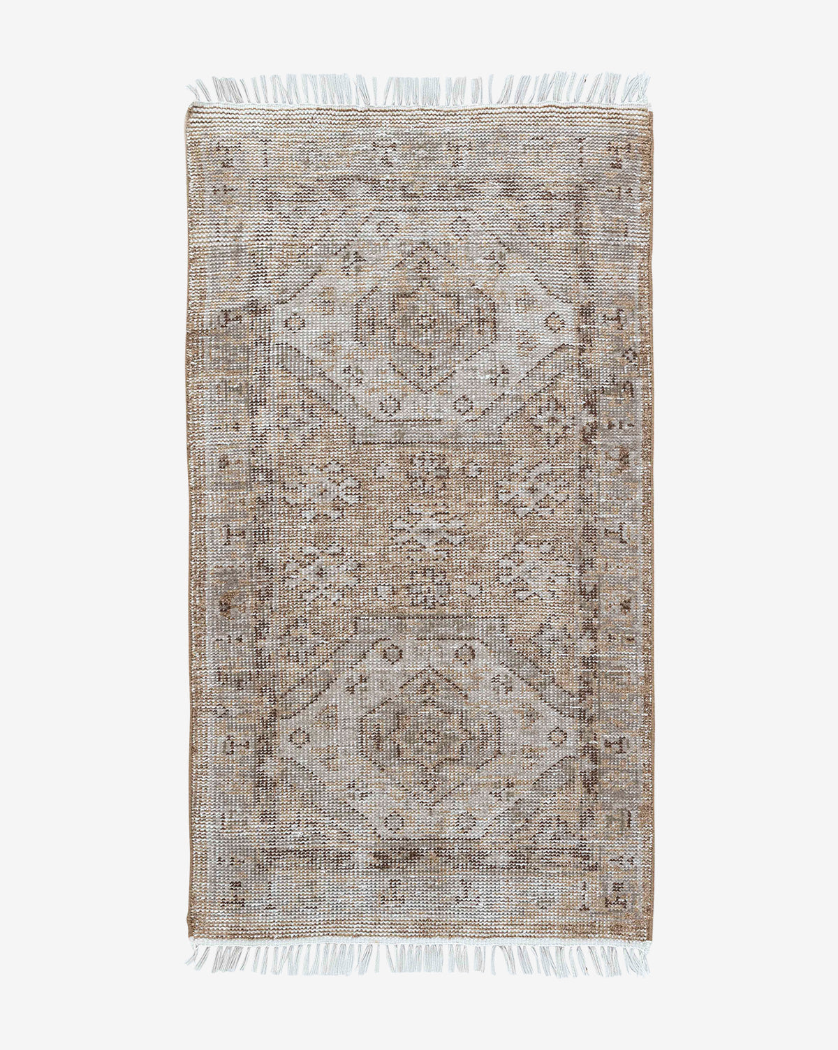The Charlot Hand-Knotted Rug is a rectangular, handmade piece featuring a faded geometric and floral pattern in muted beige, brown, and gray, finished with short white fringe on both ends for vintage style, by McGee & Co.
