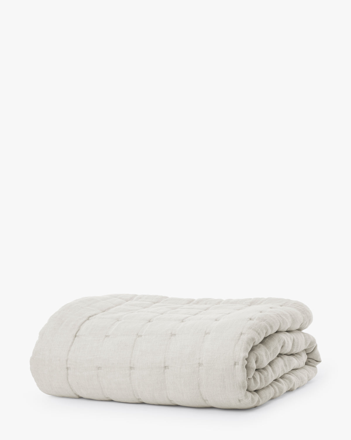 The Chaucer Quilt is a neatly folded, light grey linen-cotton quilt with quilted stitching, a soft texture, and a subtle grid pattern, displayed on a white background.