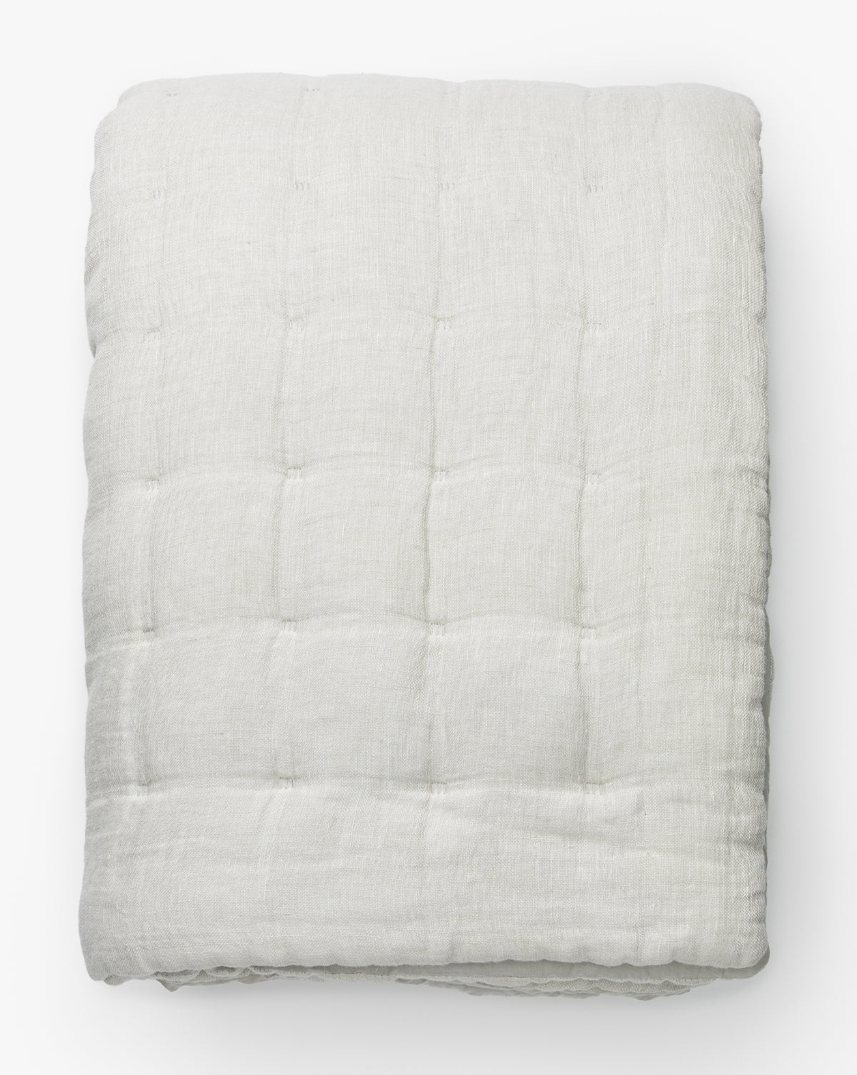 The Chaucer Quilt, shown neatly folded against a white background, is a light gray linen-cotton quilt featuring textured grid-like quilted stitching.