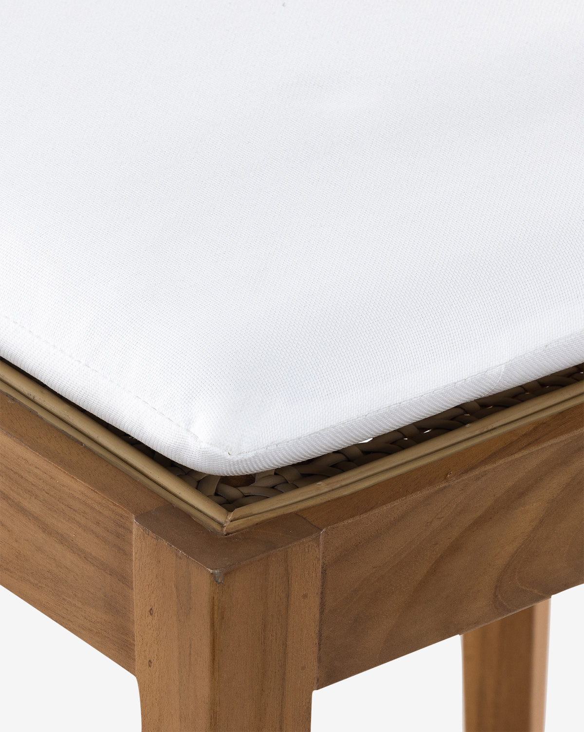 Close-up of the Chester Outdoor Dining Chair, featuring a light brown teak frame and woven rattan detail beneath a thick, white UV-resistant cushion by McGee & Co.