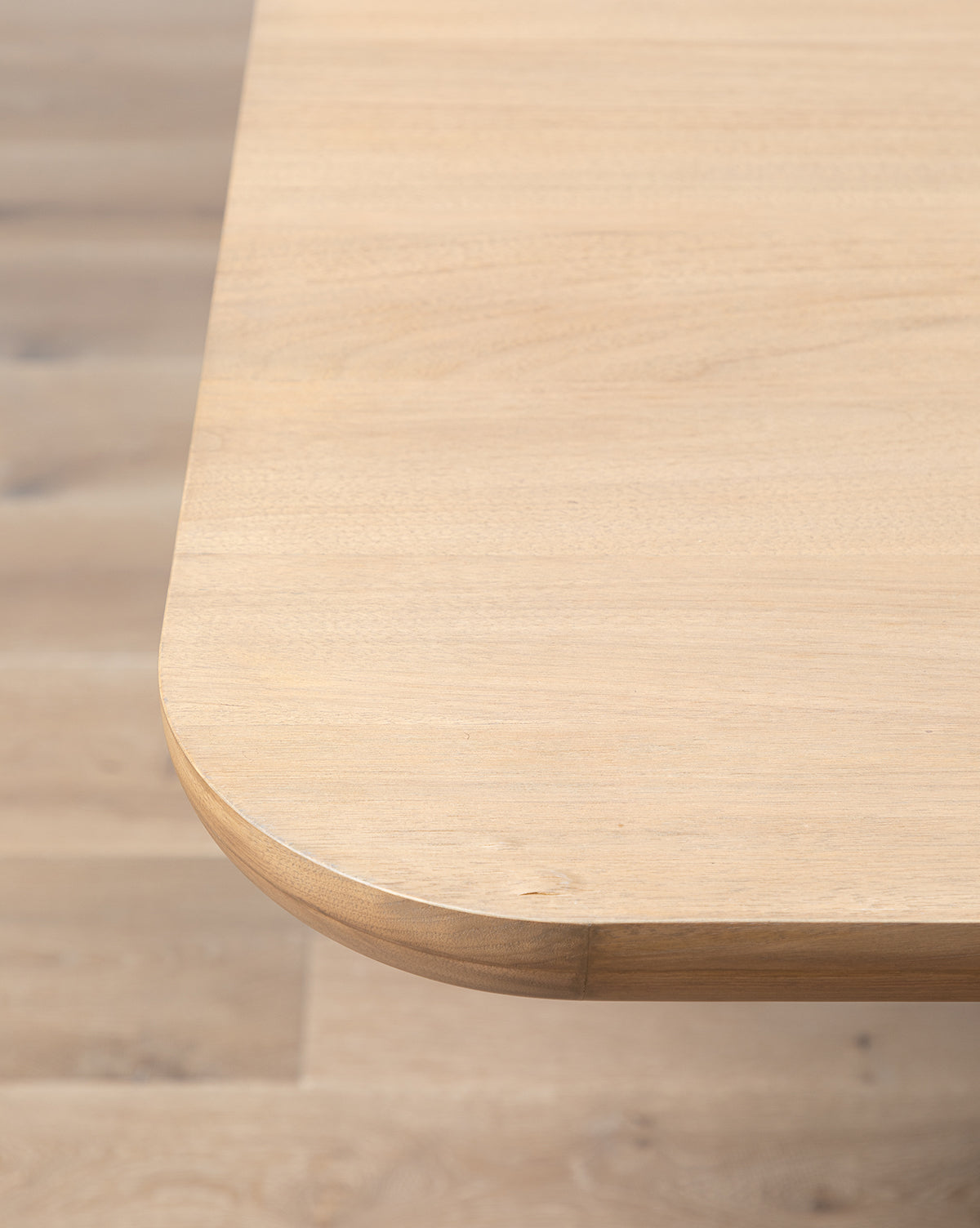 A close-up of the Cheswick Dining Tables corner highlights its modern walnut finish and rounded edges, set against a matching wooden floor, by McGee & Co.