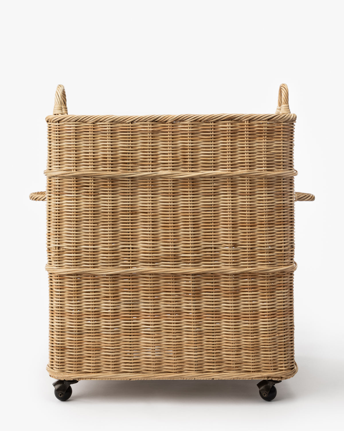 The Chiara Laundry Basket is a square, natural-finished wicker basket with side and top handles and four black caster wheels, perfect for rolling through your laundry room. Shown against a plain white background, by McGee & Co.