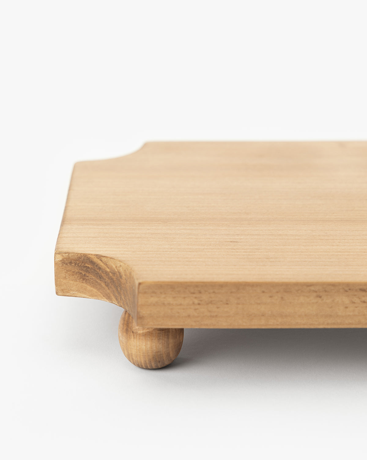 A close-up of the Cillian Pedestal Board, a rectangular pine wood board with rounded corners and small round legs, displayed on a white surface, by McGee & Co.