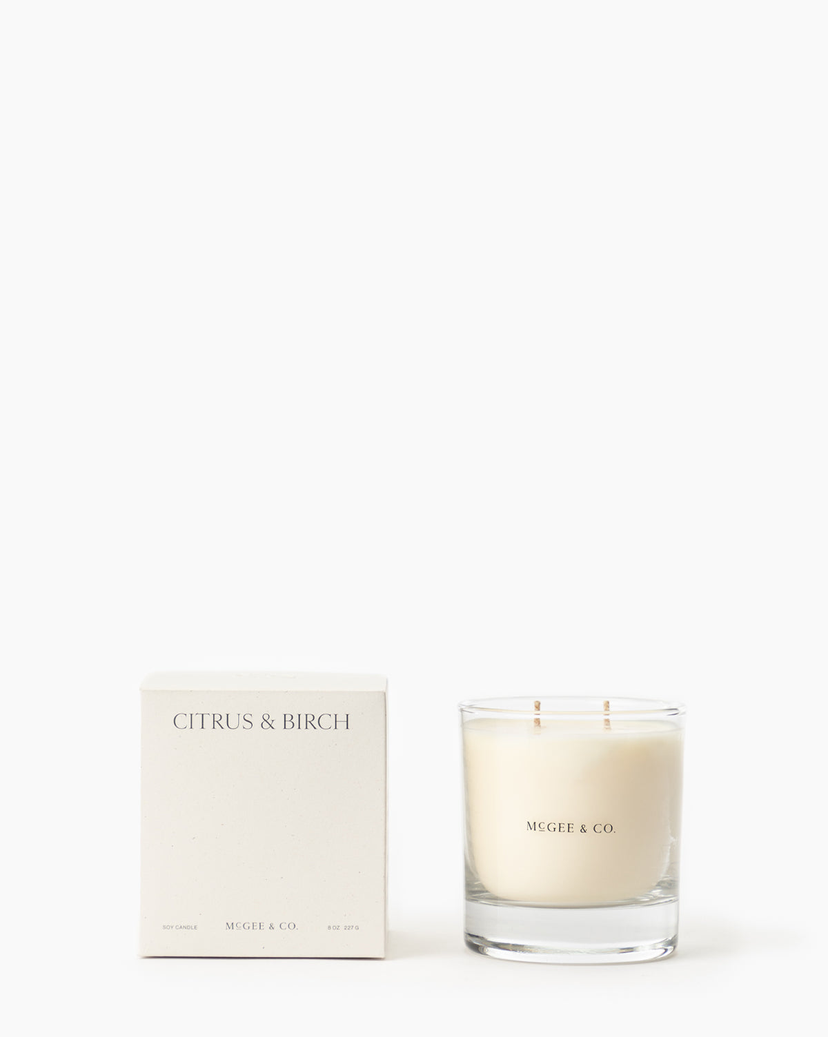 A white box labeled Citrus & Birch Candle sits beside a McGee & Co. luxury glass jar candle made from soy wax with two wicks, both displayed against a plain white background by McGee & Co.