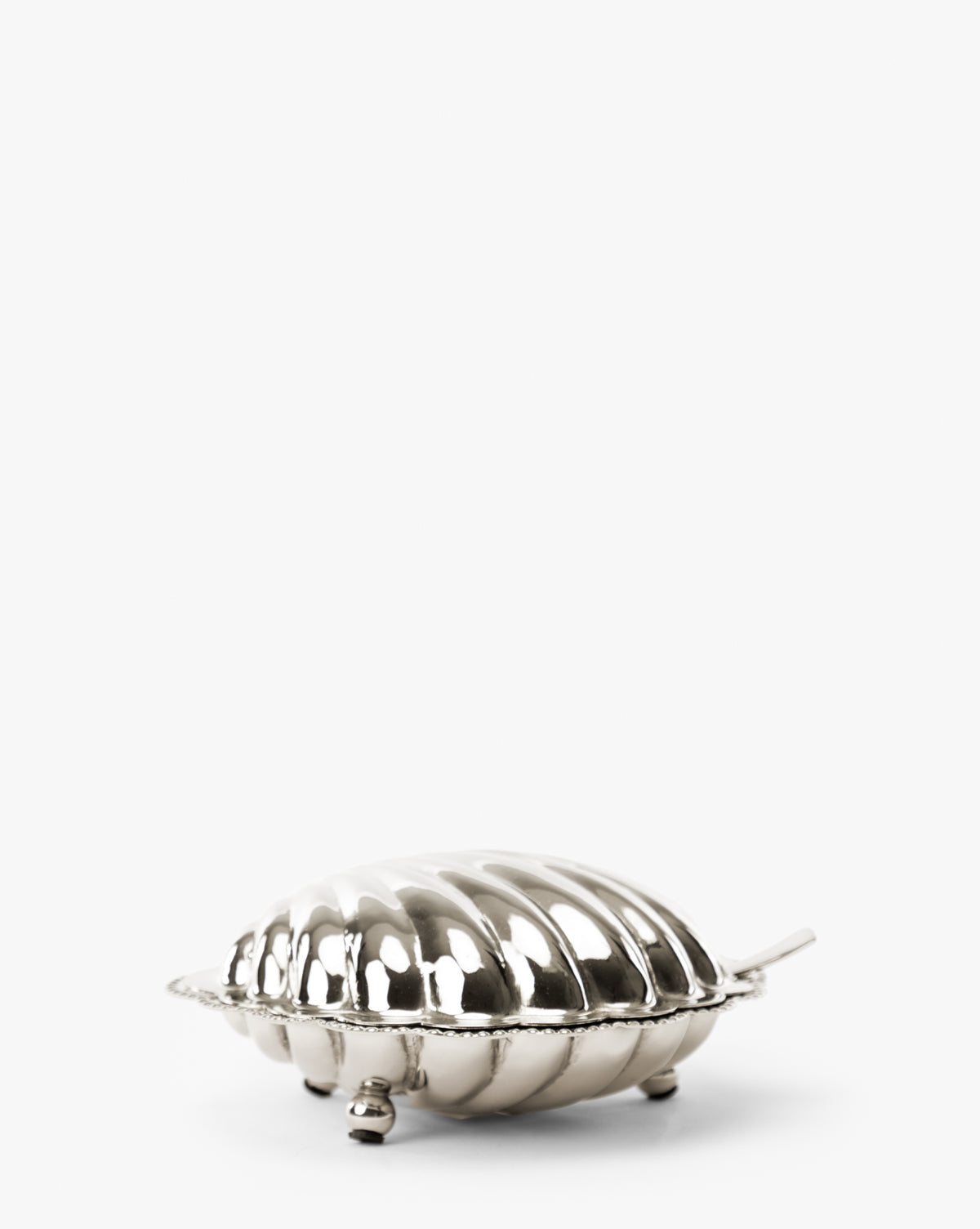 A small, shiny Clam Shell Serving Dish with Spoon, shaped like a shell with a ridged lid, three small feet, and a short handle, displayed on a plain white background, by McGee & Co.