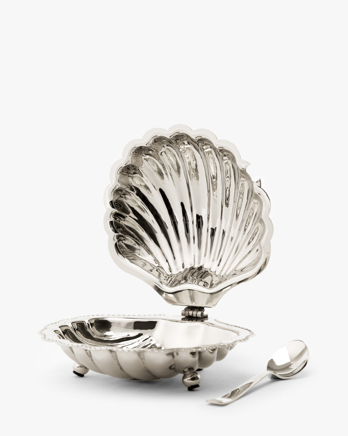 The Clam Shell Serving Dish with Spoon is open to show its reflective interior. A matching small silver spoon sits beside this elegant, hinged-lid serving dish, perfect for nautical-themed decor or entertaining by McGee & Co.